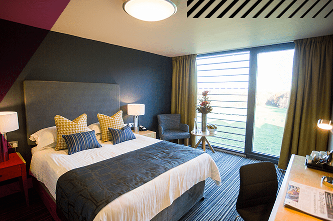 Modern bedroom with contemporary décor, double bed on the left of the room with a large glass window.