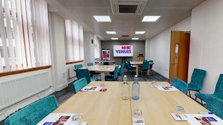 Small meeting room for seminar sessions with 3 desks and chairs set up with screen on far wall