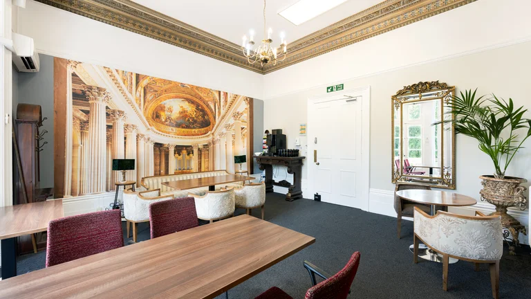 Communal seating area with chairs, armchairs and tables with tea station and baroque print on the walls