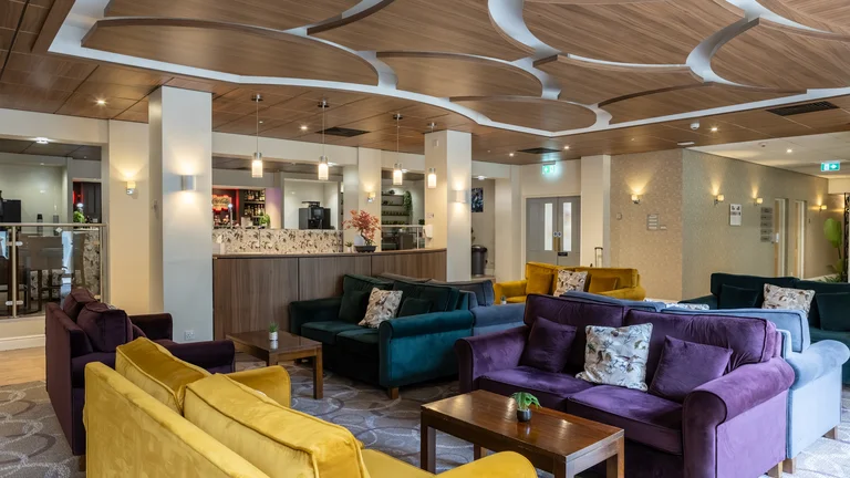 Lounge with multiple, colourful plush sofas, a coffee bar and wooden tables 