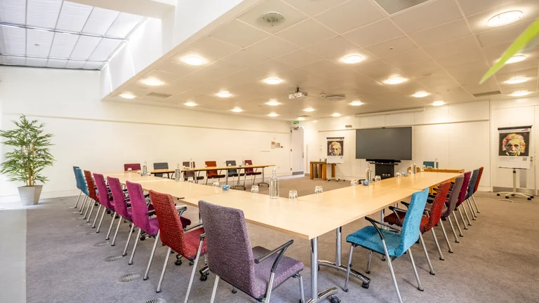 U shape desk set up surrounded by colourful chairs with screen on the wall