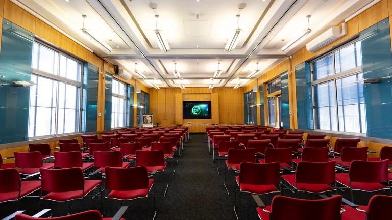 Lecture Style meeting room with chairs in rows facing screen on far wall and large windows for natural light