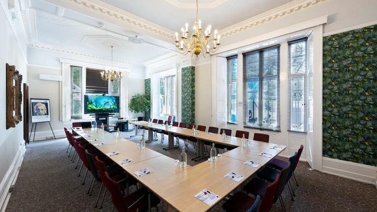 U shaped desk and chair formation with screen at front of the room, chandelier lighting and green print on walls with large windows