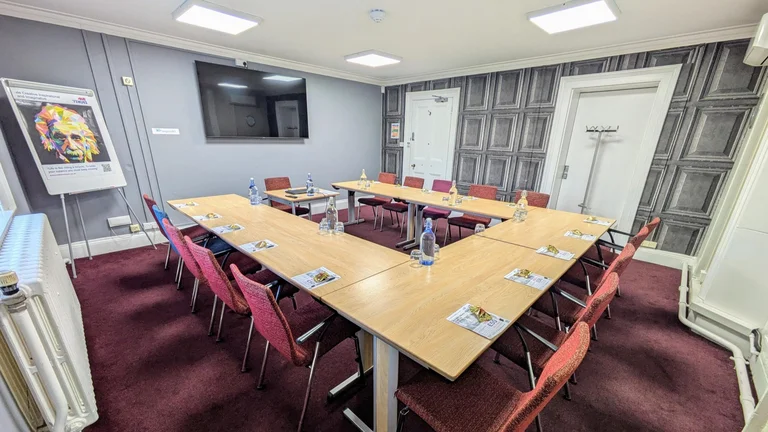 U shape arrangement of desk and chairs with panel print on walls and large screen on tv for presenting